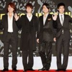 Four men in suits waving on red carpet