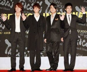 Four men in suits waving on red carpet