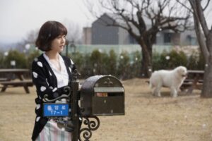 Woman by mailbox in park with white dog