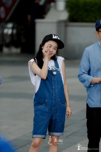 Person in denim overalls and cap posing playfully.