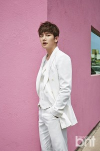 Man in white suit against pink wall.
