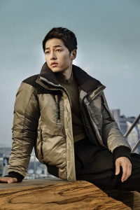 Man in puffer jacket, sitting outdoors.