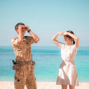 Soldier and woman shielding eyes at beach.
