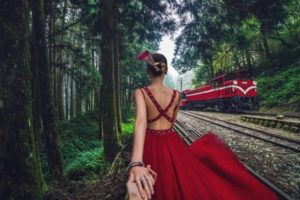 Woman in red dress by scenic train tracks.