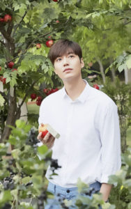 Young man holding apple in garden setting.