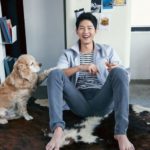 Smiling person sitting with dog on rug.