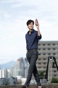 Person smiling and holding a drink outdoors.