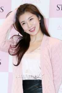 Smiling woman with long hair, pink cardigan.