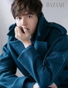 Young man in teal coat, thoughtful pose.