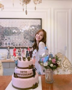 Smiling woman beside 10th anniversary cake.