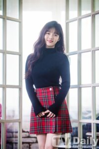 Smiling woman in black sweater and plaid skirt.