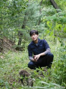 Person kneeling in a green, wooded area.