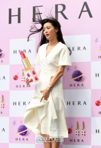 Model holding lipstick in stylish white dress.
