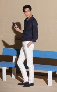 Man standing by blue bench, holding drink.