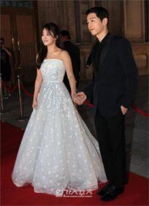 Couple holding hands on a red carpet.
