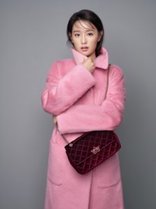 Woman in a pink coat holding a handbag.