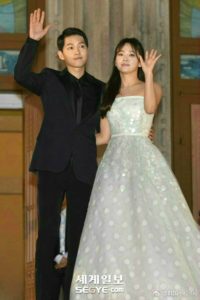 Couple waving at an event, dressed formally.