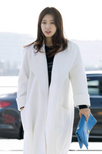 Woman in white coat holding blue clutch.