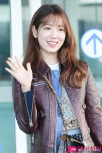 Smiling person waving in a casual outfit.