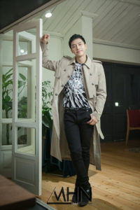 Man in a trench coat leaning by a door.