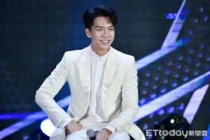 Smiling man in a white suit on stage.