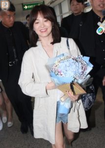 Woman holding bouquet and smiling at airport.