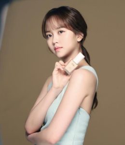 Woman holding foundation bottle, neutral background.