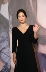 Woman in black dress waving at event.