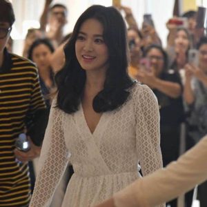 Woman in a white dress smiling at crowd.
