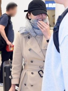 Person in a trench coat and scarf smiling.