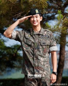 Smiling soldier giving a salute outdoors.