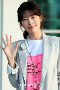 Smiling person waving in casual attire.