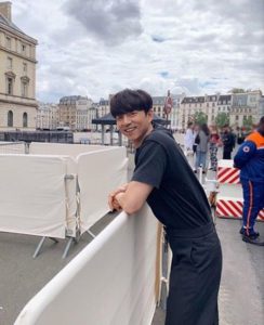 Smiling man leaning on a barrier outdoors.