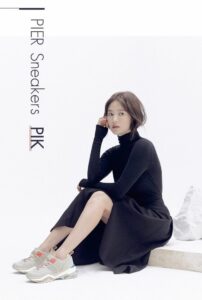 Model sitting with stylish sneakers and dress.