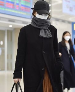 Person in black coat and scarf at airport.