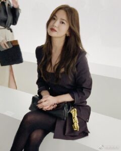 Woman sitting, wearing stylish black outfit.