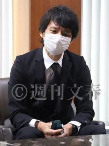 Man in suit and mask sitting pensively.