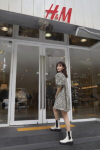 Woman in leopard dress outside H&M store.