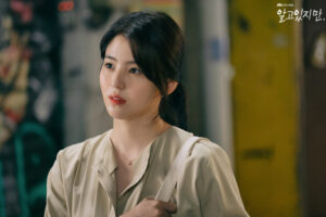 Woman in a light blouse, thoughtful expression.