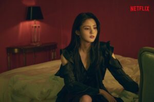 Woman sitting on bed in dimly lit room.