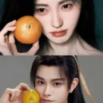 Two figures holding oranges beside their faces.