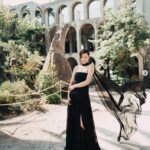Woman in black dress, outdoor architectural setting.