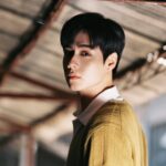 Person standing under a rustic roof structure.