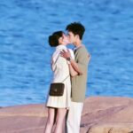 Couple kissing on rocky shore by ocean.