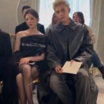 Fashionably dressed couple seated at event.