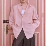 Man in pink shirt, standing against door.