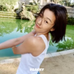 Woman smiling near a green pond outdoors.