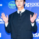 Person waving at an event, blue background.