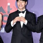 Man in tuxedo making heart gesture.