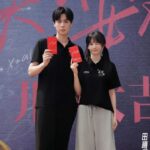 Two people holding red envelopes, smiling.